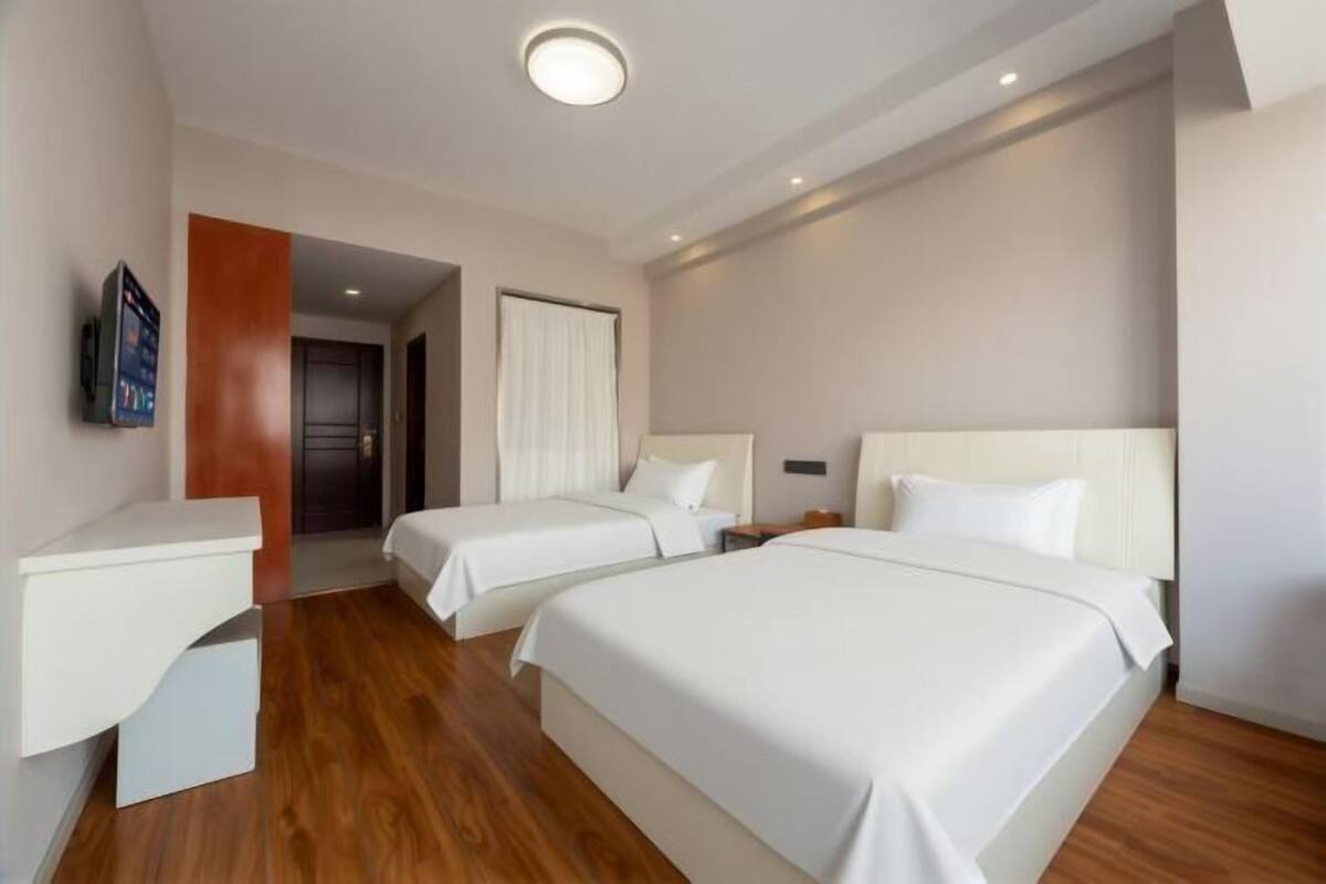 Une chambre d’hôtel avec deux lits, un bureau, une télévision et une porte donnant sur une autre pièce.