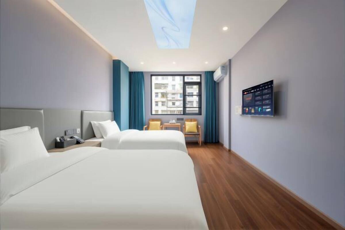 Une chambre d’hôtel avec deux lits, un bureau, une chaise, une télévision et une fenêtre avec des rideaux.