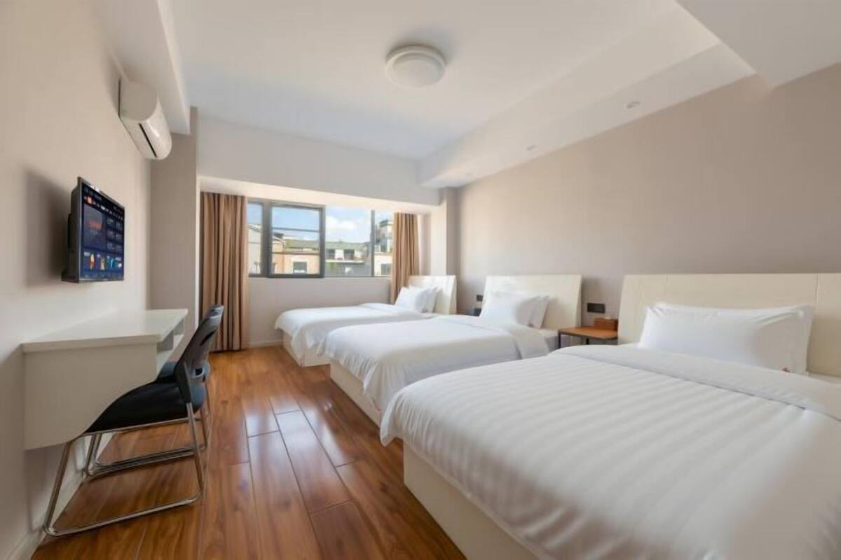 Une chambre d’hôtel avec deux lits, un bureau, une chaise, une télévision et une fenêtre donnant sur des immeubles.