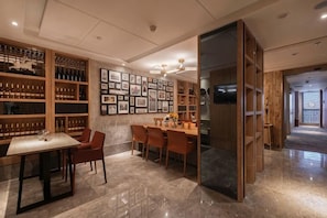 Uma área de refeições com piso de mármore, cadeiras de madeira, uma mesa e um aparador de vinhos com garrafas.