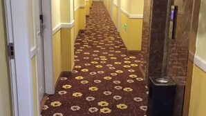 Ein Hotelgang mit Teppichmuster, Türen und einem Mülleimer.