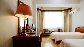 Una habitación de hotel con dos camas, un escritorio con lámpara, televisión y una silla.