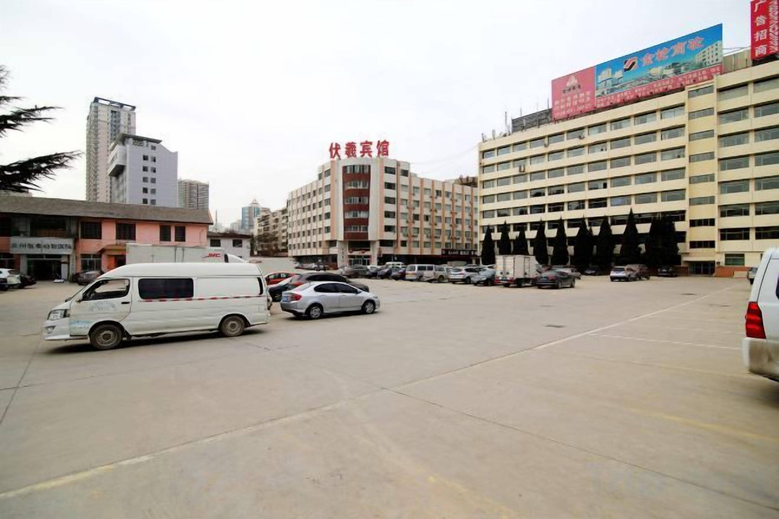 Ein Parkplatz mit mehreren Fahrzeugen, ein Gebäude mit einer Beschilderung und eine größere Struktur mit einem roten Banner.