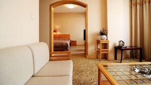 Habitación de hotel con sofá, cama, una mesita con un florero, una silla de madera y un escritorio con tetera.