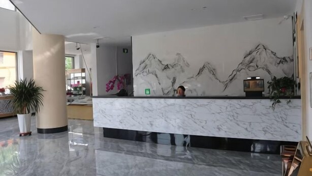 Zona de recepción de hotel con mostrador de mármol, un mural de montañas y una planta en maceta.