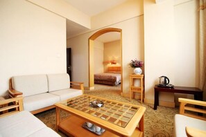 A hotel room with a sofa, a coffee table, a bed, a mirror, a small table with a kettle, and a flower vase. - Lanzhou Fuxi Hotel (Lanzhou)