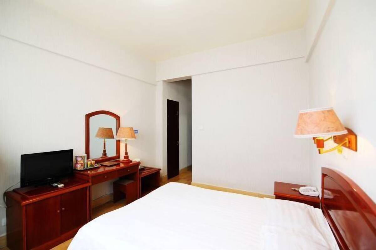 A hotel room with a bed, a desk with a TV, a mirror, and a lamp.