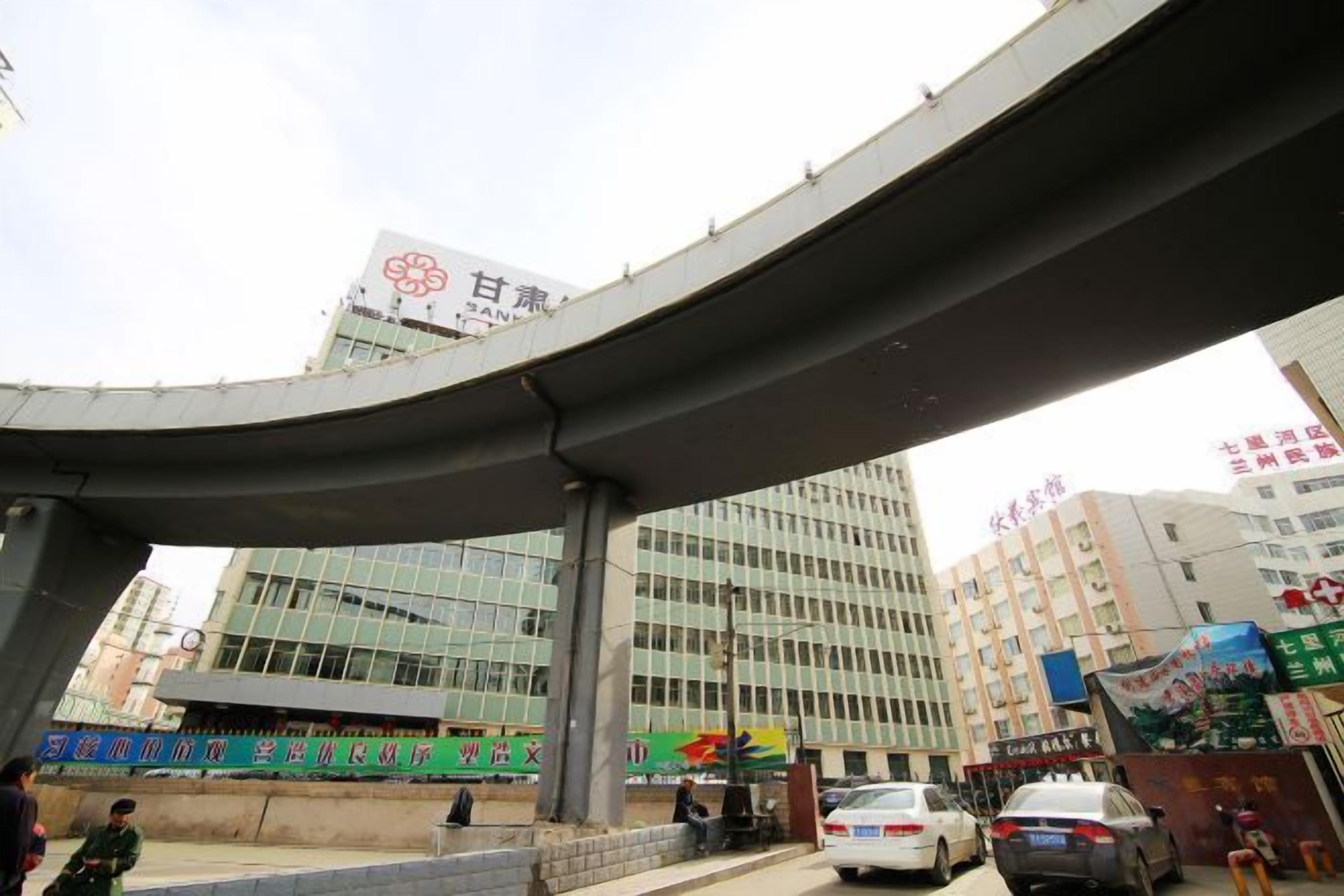 Egy modern épület, amelynek része egy ívelt felüljáró, nagyméretű üveg homlokzat és egy kínai karakterekkel ellátott tábla.