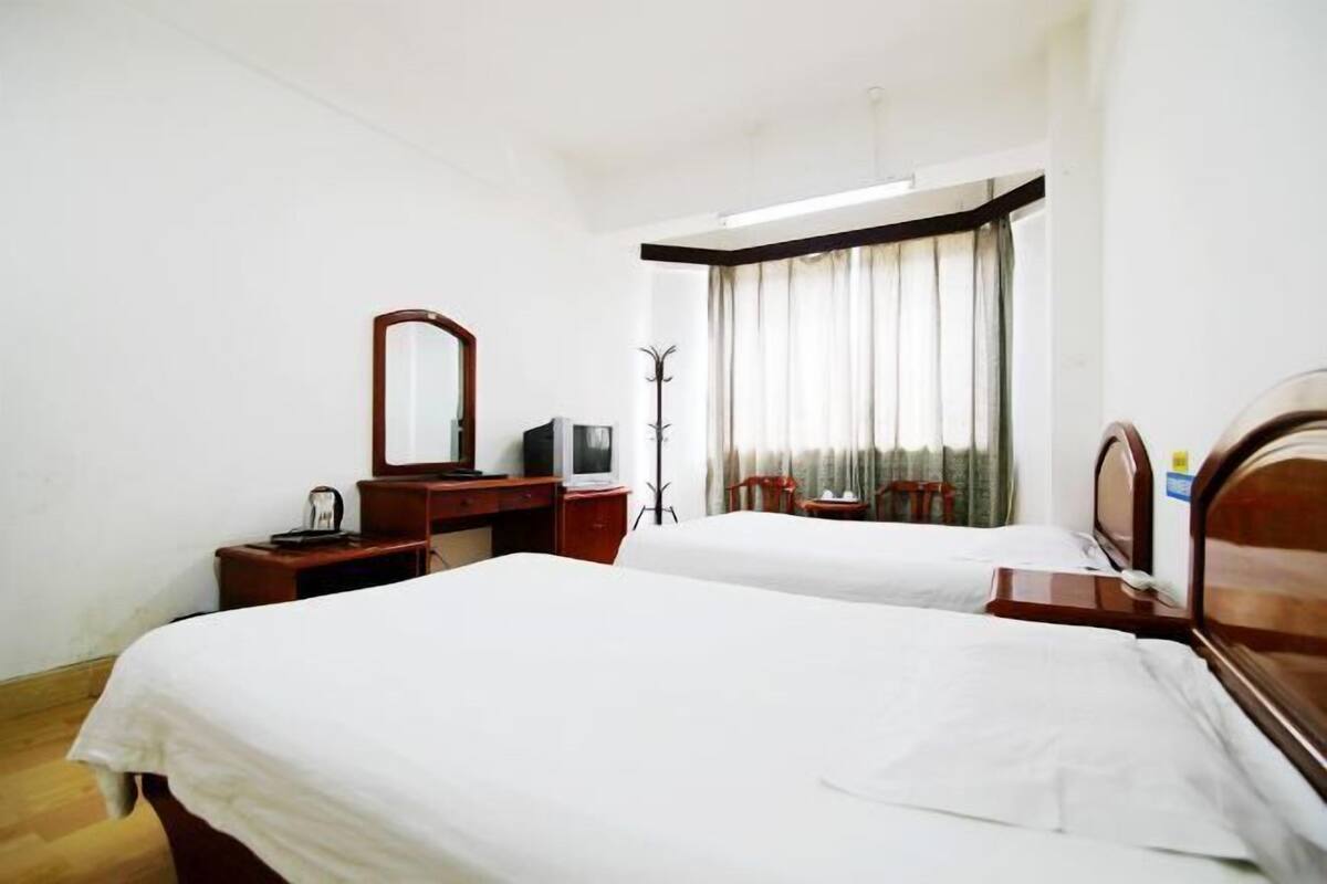 A hotel room with two beds, a desk with a chair, a mirror, a coat stand, and a window with curtains.