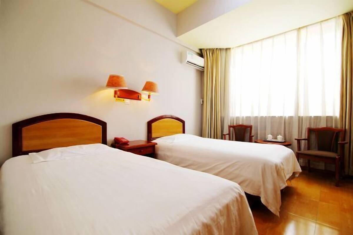 A hotel room with two beds, a nightstand, a chair, and a window with curtains.