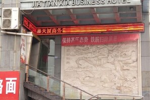 A hotel entrance with a red sign, a staircase, and a relief sculpture. - Jiatianxia Business Hotel (Pingliang)