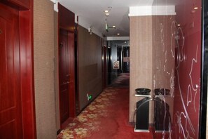 A hotel corridor with wooden doors, a red carpet, and a trash bin. - Jiatianxia Business Hotel (Pingliang)