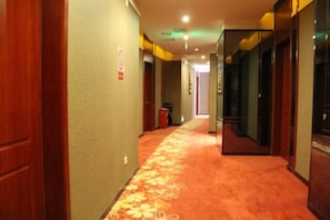 A hotel corridor with carpeted flooring, doors on both sides, and a trash bin in the center. - Jiatianxia Business Hotel (Pingliang)