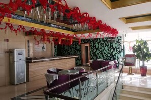 Een hotellobby met een receptiebalie, zithoek en een trap.