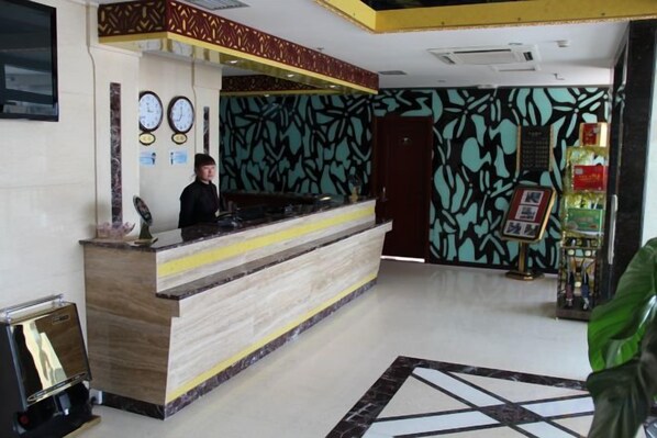 Zona de recepción de un hotel con mostrador de mármol, relojes y una pared con diseño.