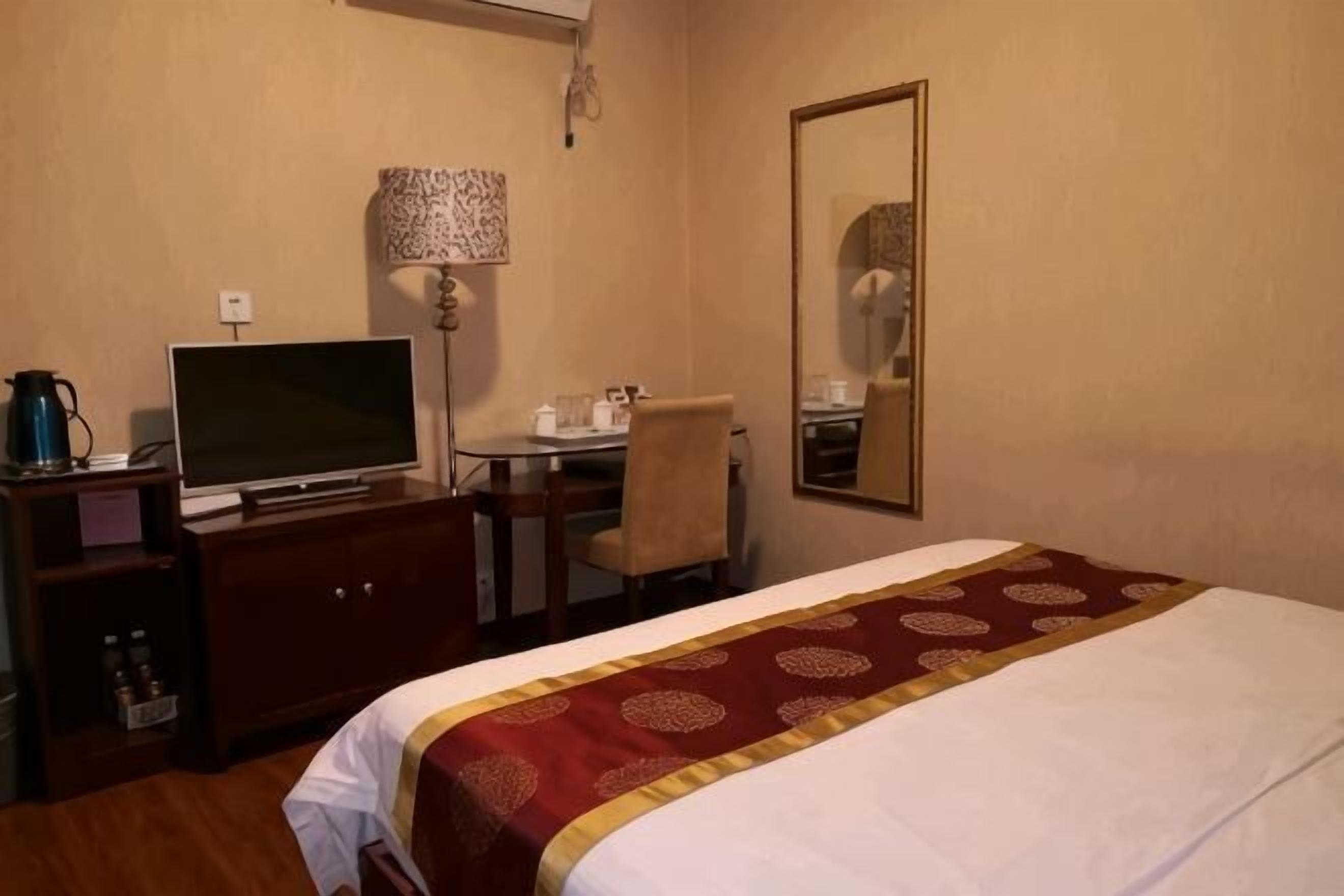 A hotel room with a bed, a desk with a chair, a television, and a mirror.