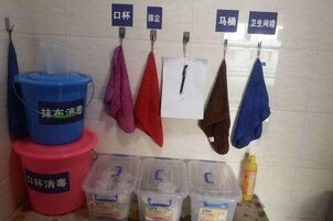 A bathroom with hand towels hanging on hooks, labeled in Chinese. There are also plastic containers with labels and a bottle on the counter.