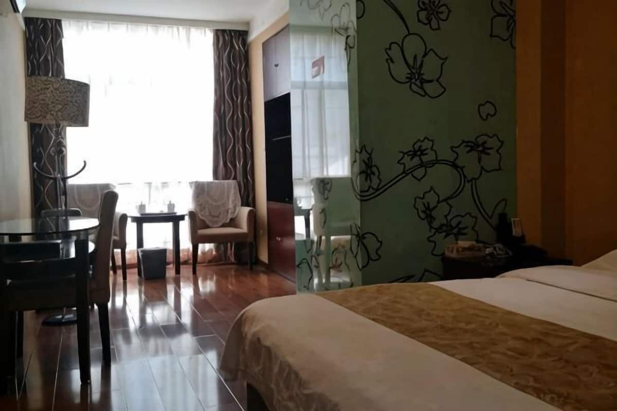 A hotel room with a bed, a desk, a chair, a lamp, and a window with curtains.