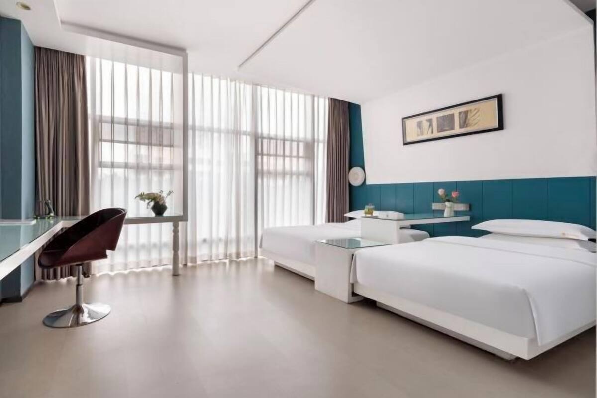Ein Hotelzimmer mit Bett, Schreibtisch, Stuhl, kleinem Tisch und einem Fenster mit Vorhängen.