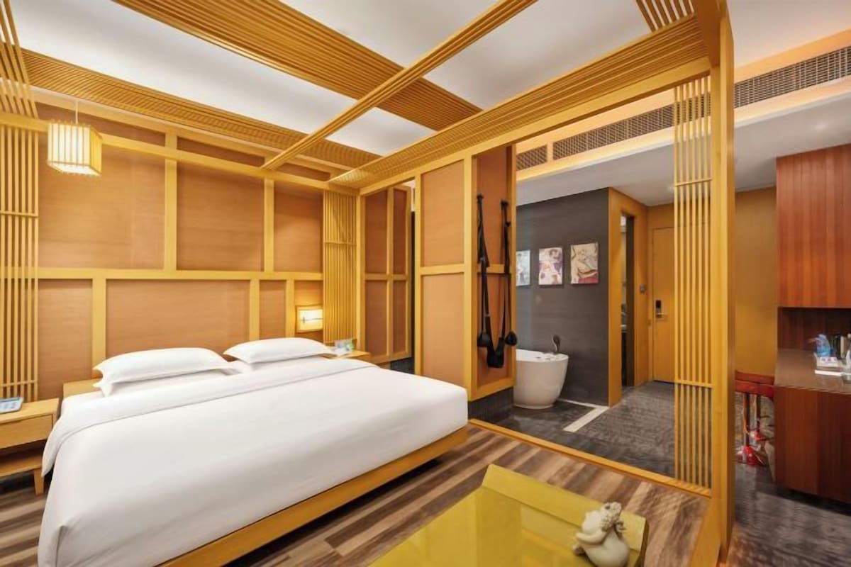 Habitación de hotel con una cama grande, una mesita pequeña y un baño con bañera.