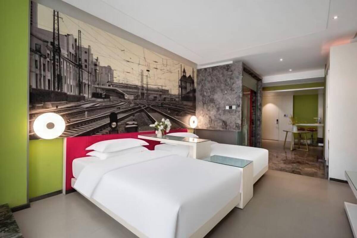 Ein modernes Hotelzimmer mit einem großen Bett, Nachttischen, einem Wandbild einer Stadtansicht und einer separaten Sitzecke.