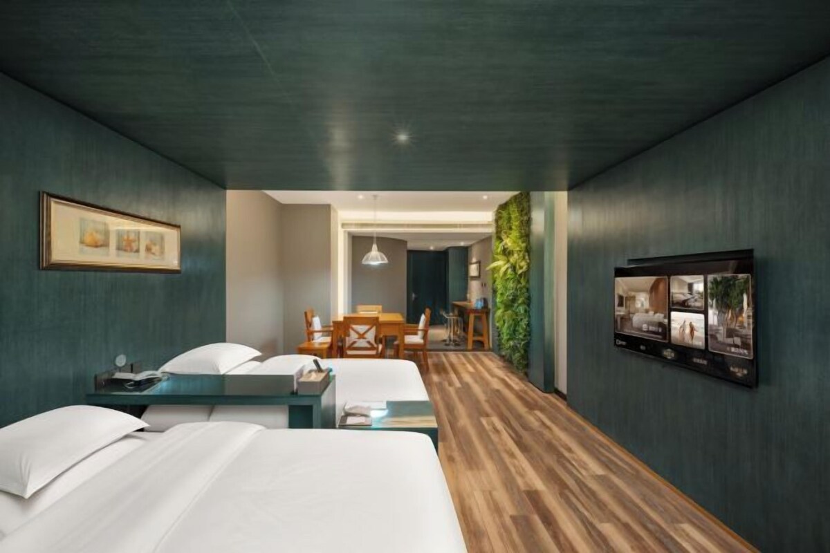 Una habitación de hotel con cama, mesita de noche y escritorio. Hay una zona de comedor con una mesa y sillas.
