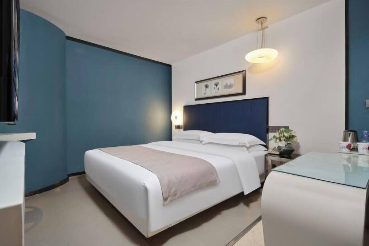 Ein Hotelzimmer mit Bett, Nachttisch, Lampe und einem gerahmten Bild an der Wand.