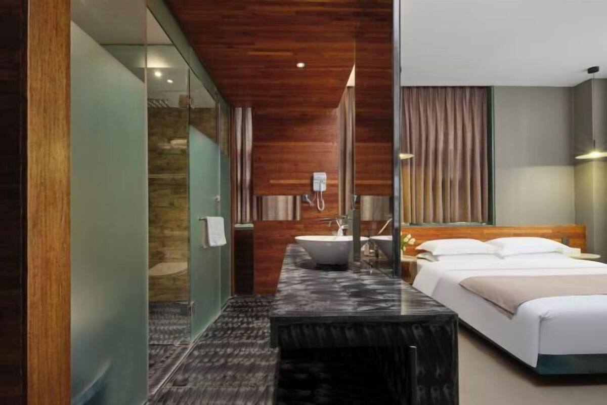 Ein modernes Hotelzimmer mit einem großen Bett, einem Badezimmer mit einer Badewanne und einer Glasabtrennung.