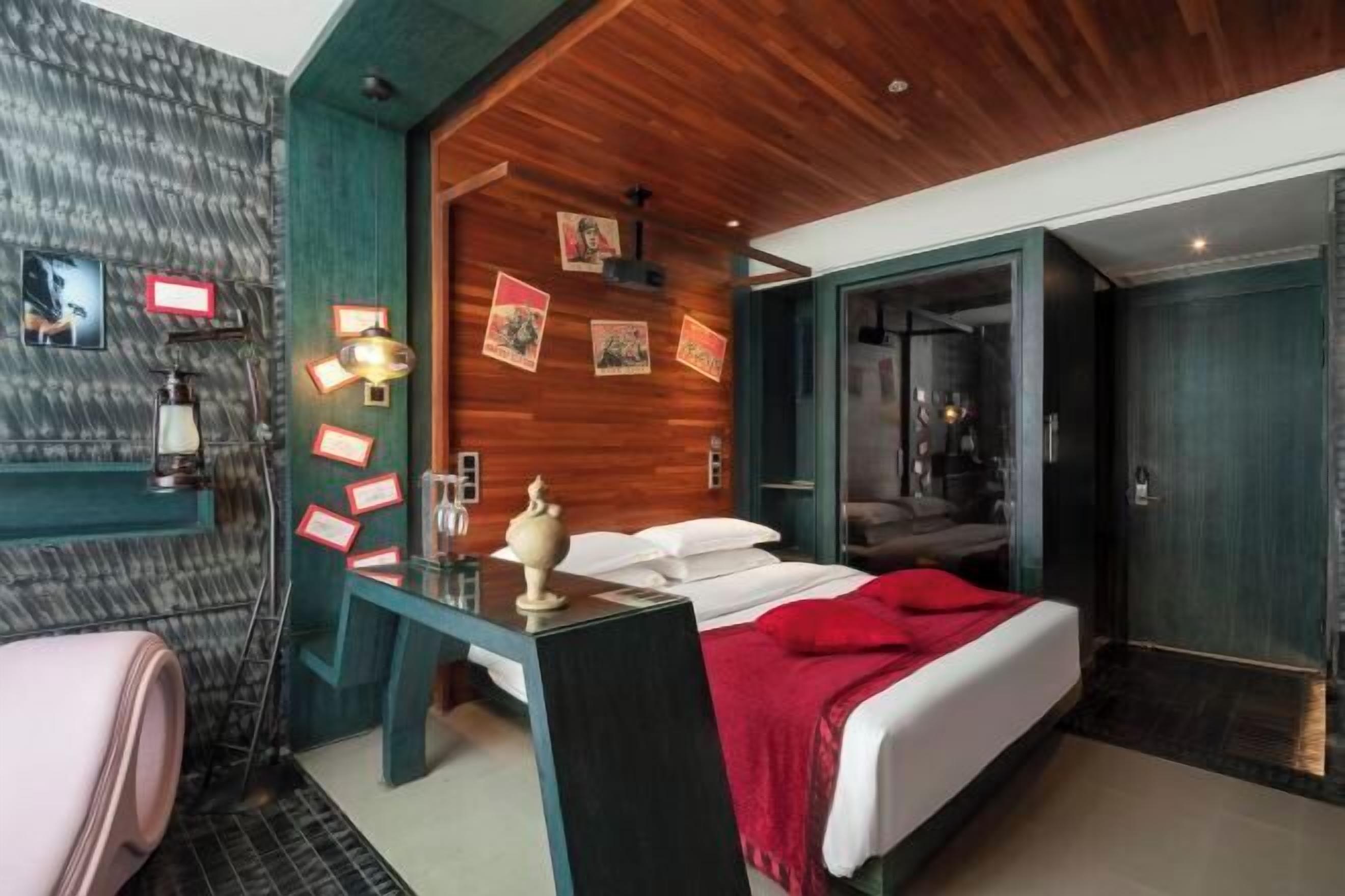 A hotel room with a bed, a desk, a chair, a vanity with a mirror, and a door leading to another room.