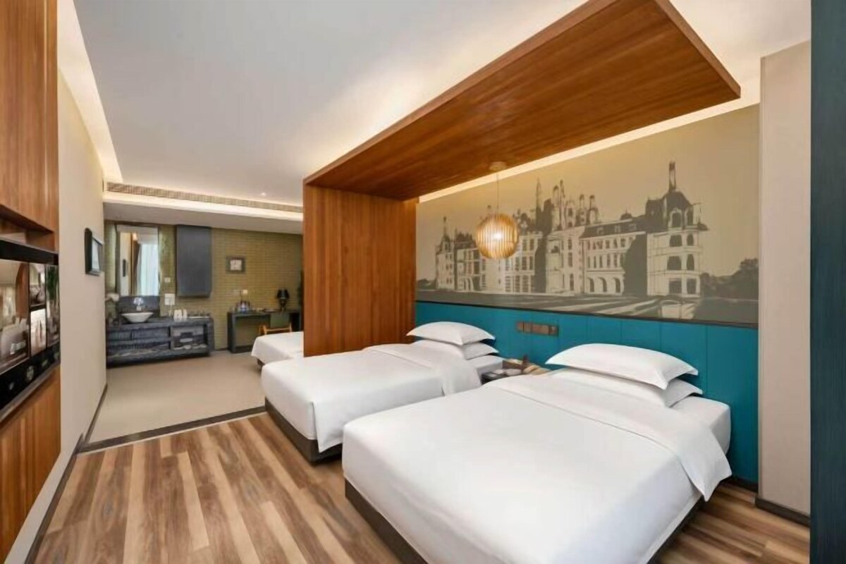 Habitación de hotel con dos camas, un mural con vista a la ciudad, techo de madera y una kitchenette al fondo.