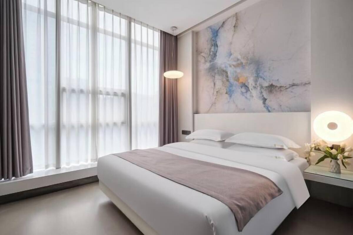 Ein modernes Hotelzimmer mit einem großen Bett, einem Wandbild und einem Nachttisch mit einer Lampe.