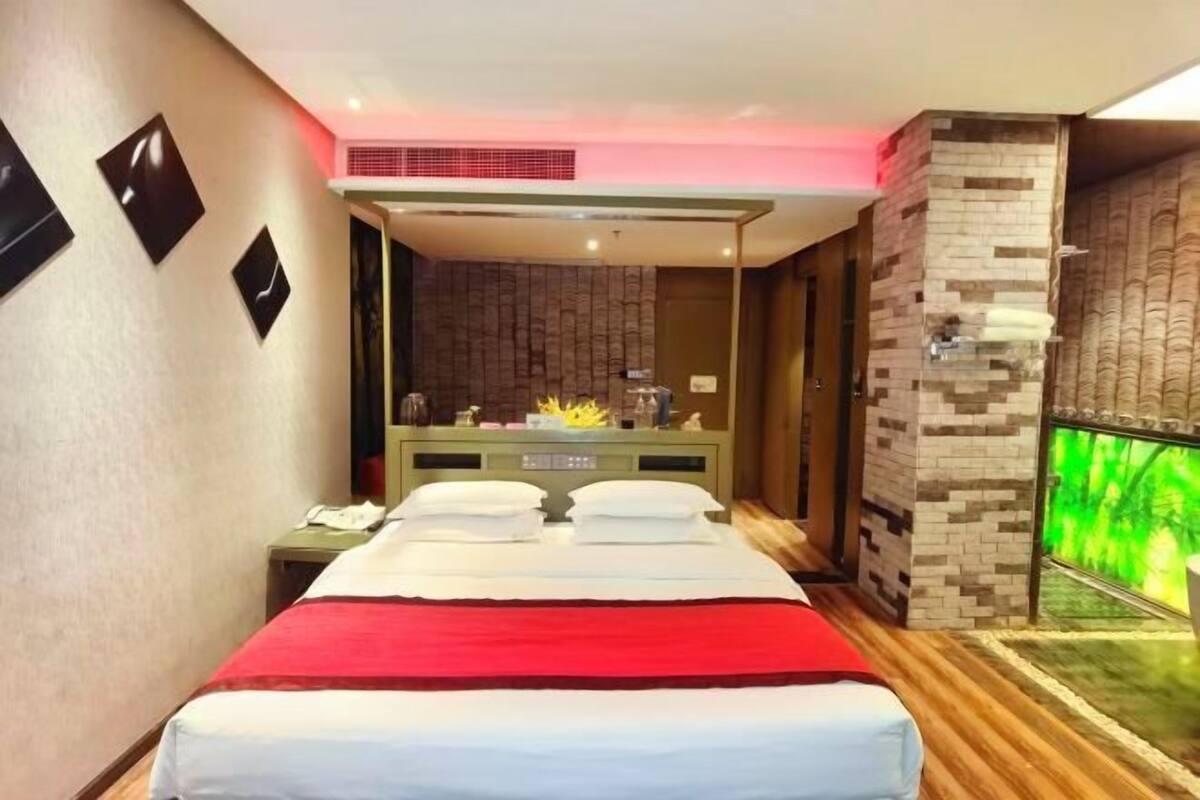 Ein Hotelzimmer mit Bett, Nachttisch, Spiegel, Wandfernseher und einer Wand aus Stein.