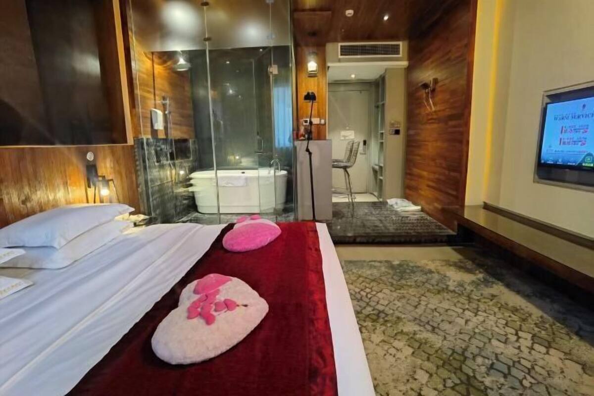 Ein Hotelzimmer mit einem großen Bett, einer Glaskabine für die Dusche und einem an der Wand befestigten Fernseher.