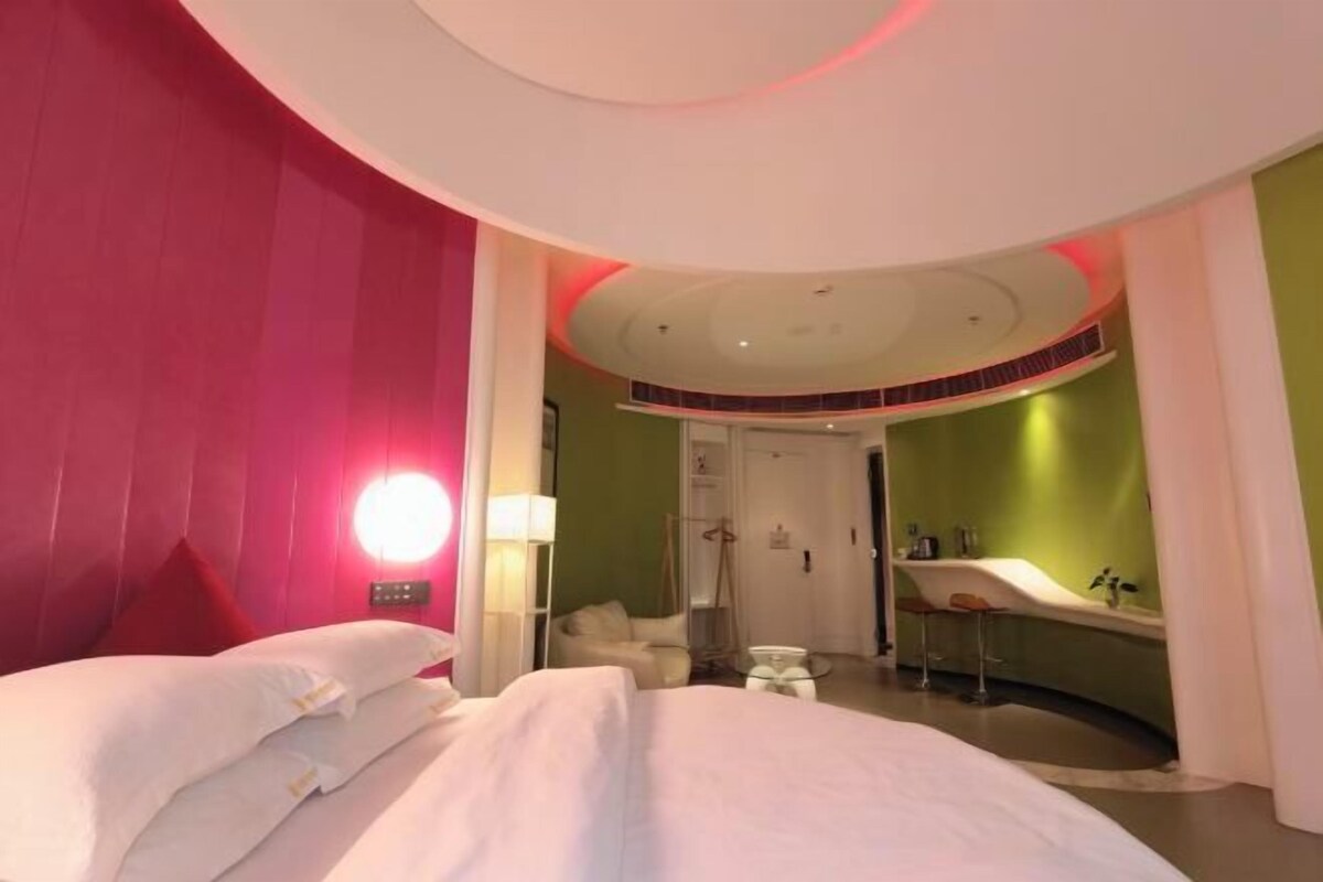 A modern hotel room with a large bed, a sitting area, and a bathroom with a bathtub.