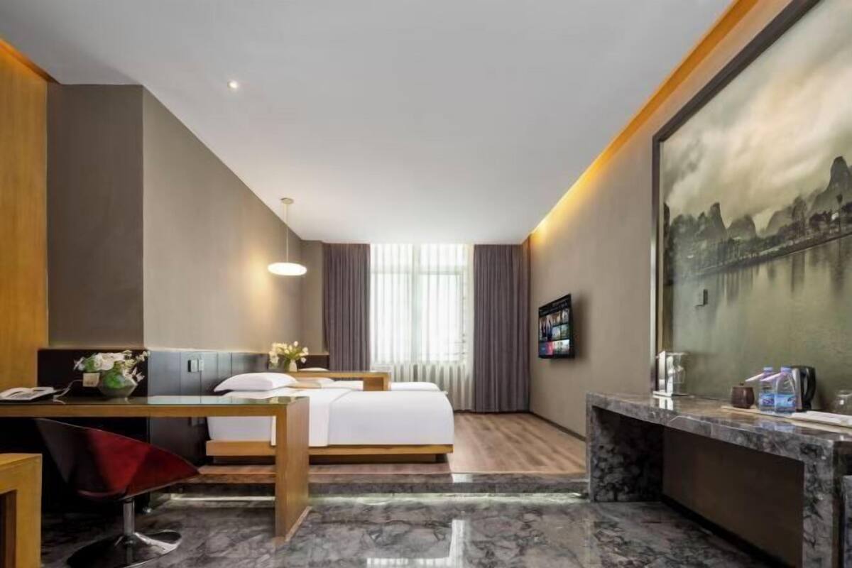 Ein Hotelzimmer mit Bett, Schreibtisch, Stuhl und einem großen Gemälde an der Wand.