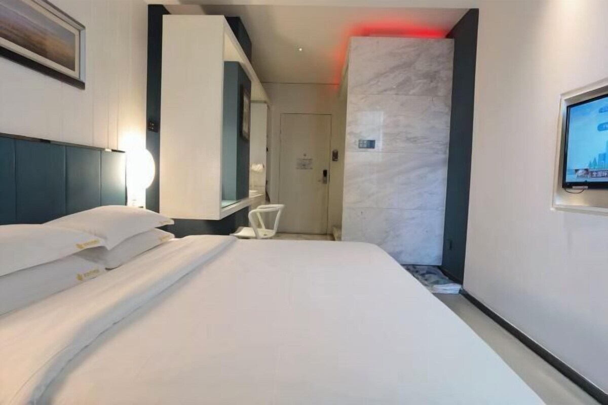 A hotel room with a bed, a TV mounted on the wall, a marble accent wall, and a door leading to another room.