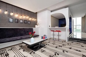 A modern living room with a dark sofa, a coffee table with a vase of flowers, a bar area, and a patterned floor. - Mianyang 4D Future Hotel (Gaoshui Branch) (Mianyang)
