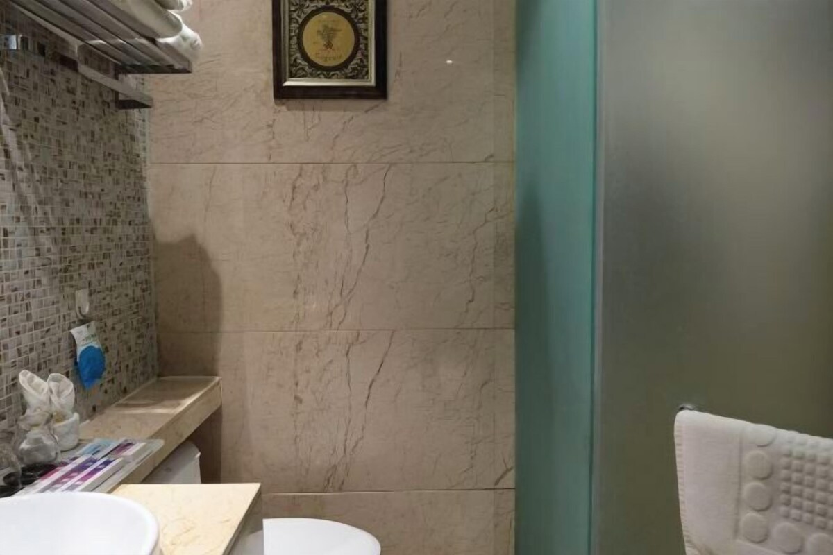 A bathroom with a marble wall, a sink, a towel rack, and a framed certificate on the wall.