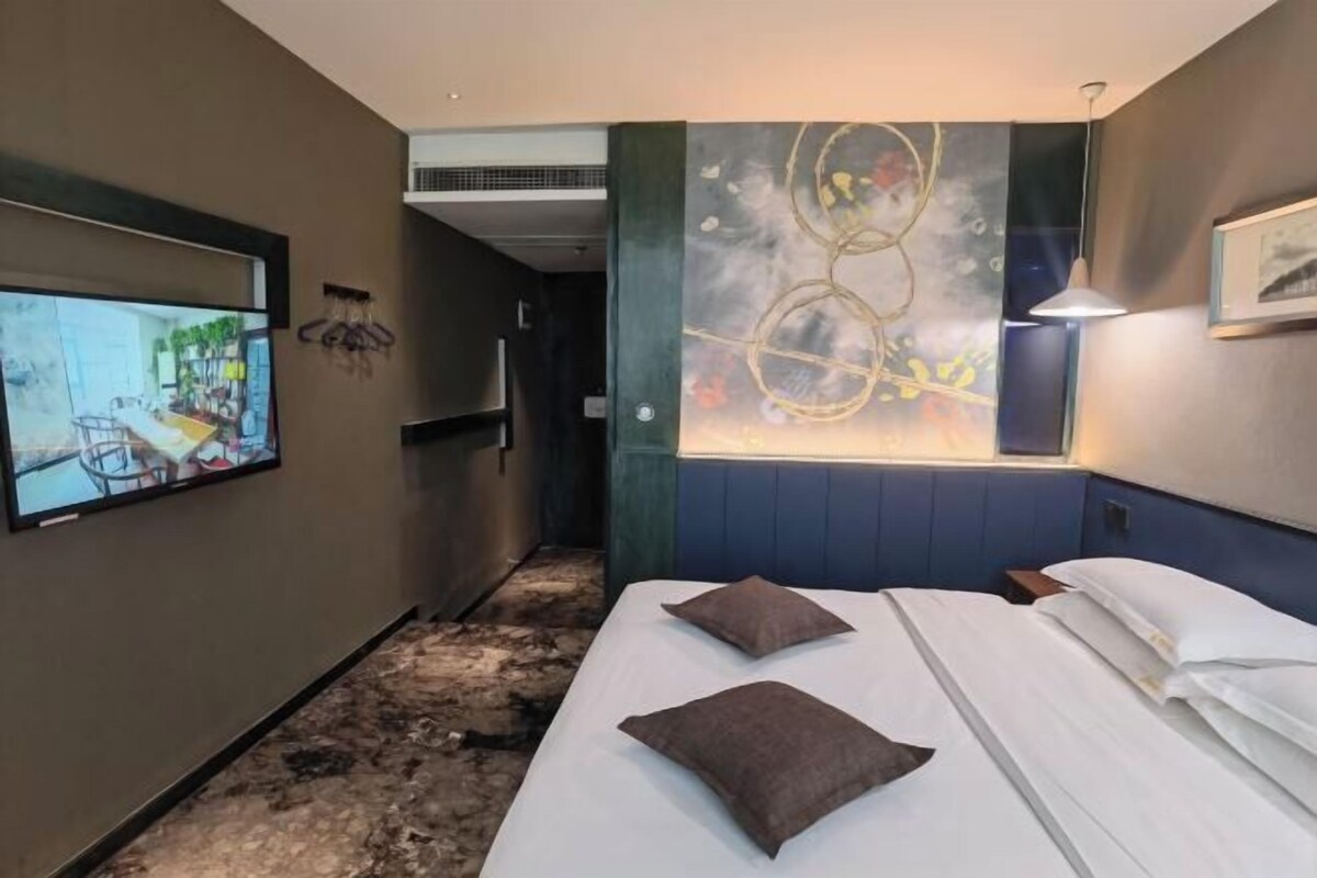 A hotel room with a bed, a TV mounted on the wall, and a window with a view of the outside.