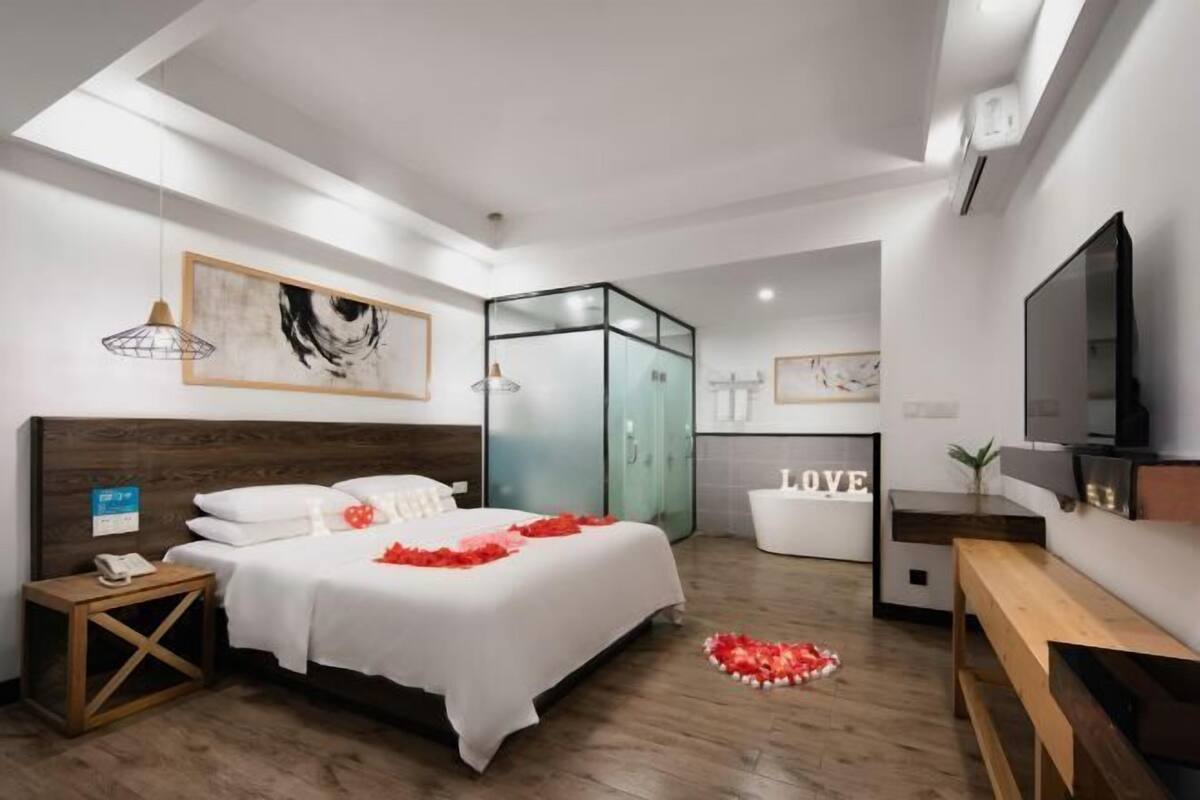 Habitació d'hotel moderna amb un llit gran, una taula de treball, un televisor i una separació de vidre.