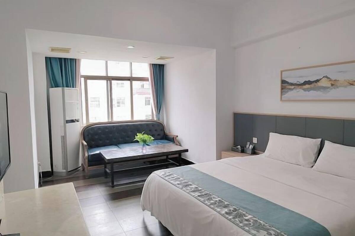 Habitació d'hotel amb llit, sofà, taula, televisió i finestra amb cortines.