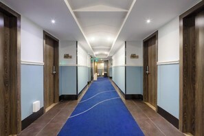 A hotel hallway with a blue carpet, wooden doors, and a ceiling with recessed lighting. - Time Inn (Wenchang)
