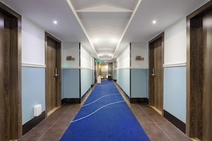 Un pasillo de hotel con alfombra azul, puertas de madera e iluminación empotrada en el techo.