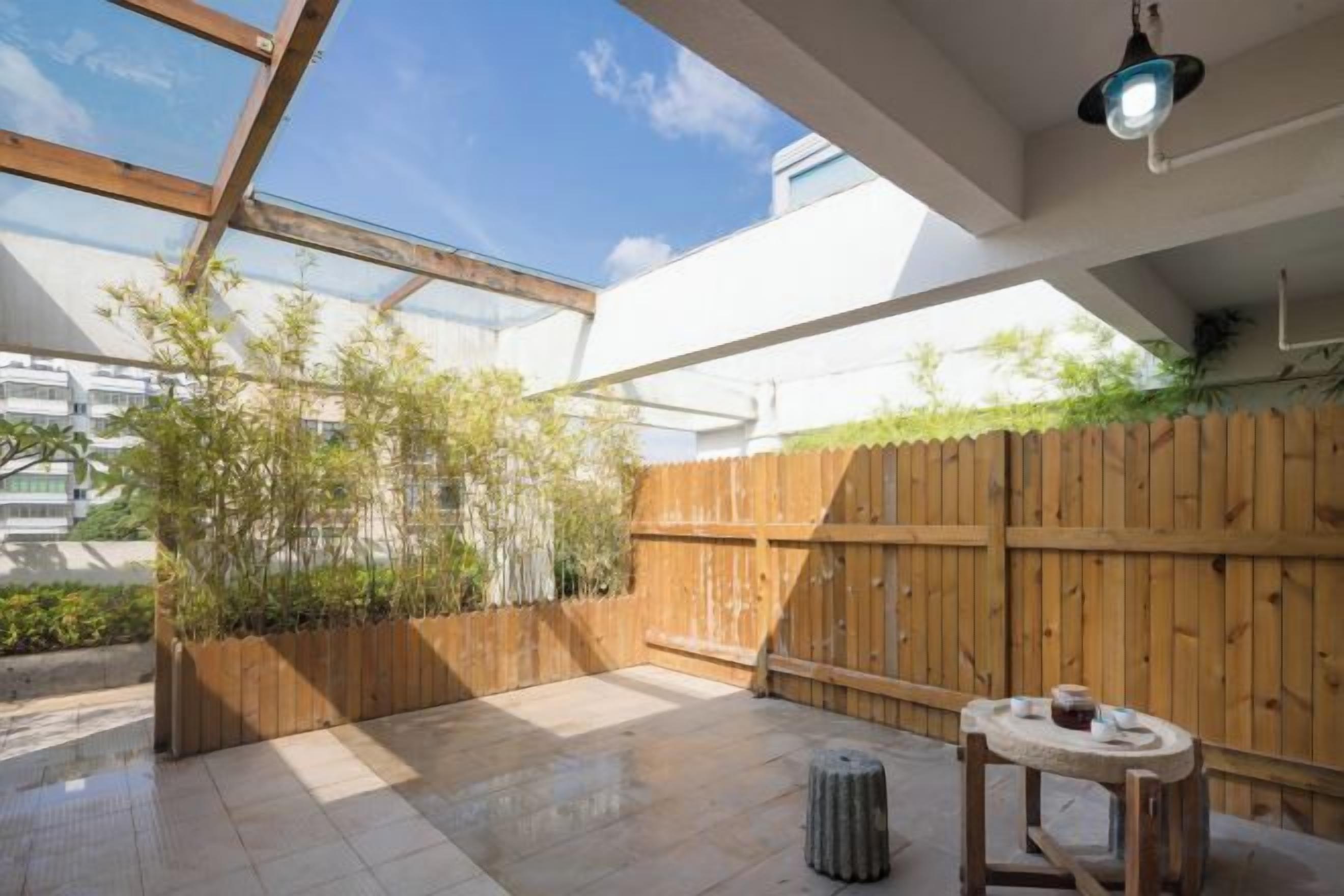 Um pátio externo com cerca de madeira, uma mesa e um lustre suspenso.