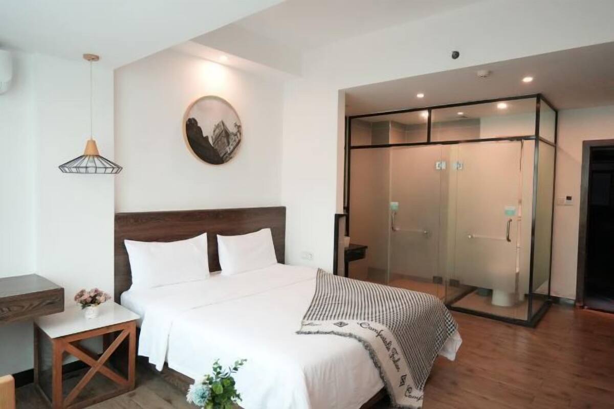 Habitació d'hotel moderna amb un llit, una taula de nit i una zona de banyera amb dutxa tancada amb vidre.