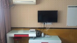 A room with a flat-screen TV mounted on the wall, a white desk with a red stool, and an air conditioning unit above the desk. - Xingsheng Hostel (Shanghai)