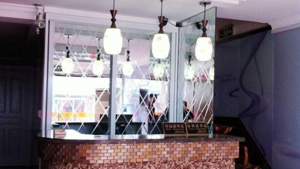 A reception area with a brick counter, hanging pendant lights, and a large mirror above the counter. - Xingsheng Hostel (Shanghai)