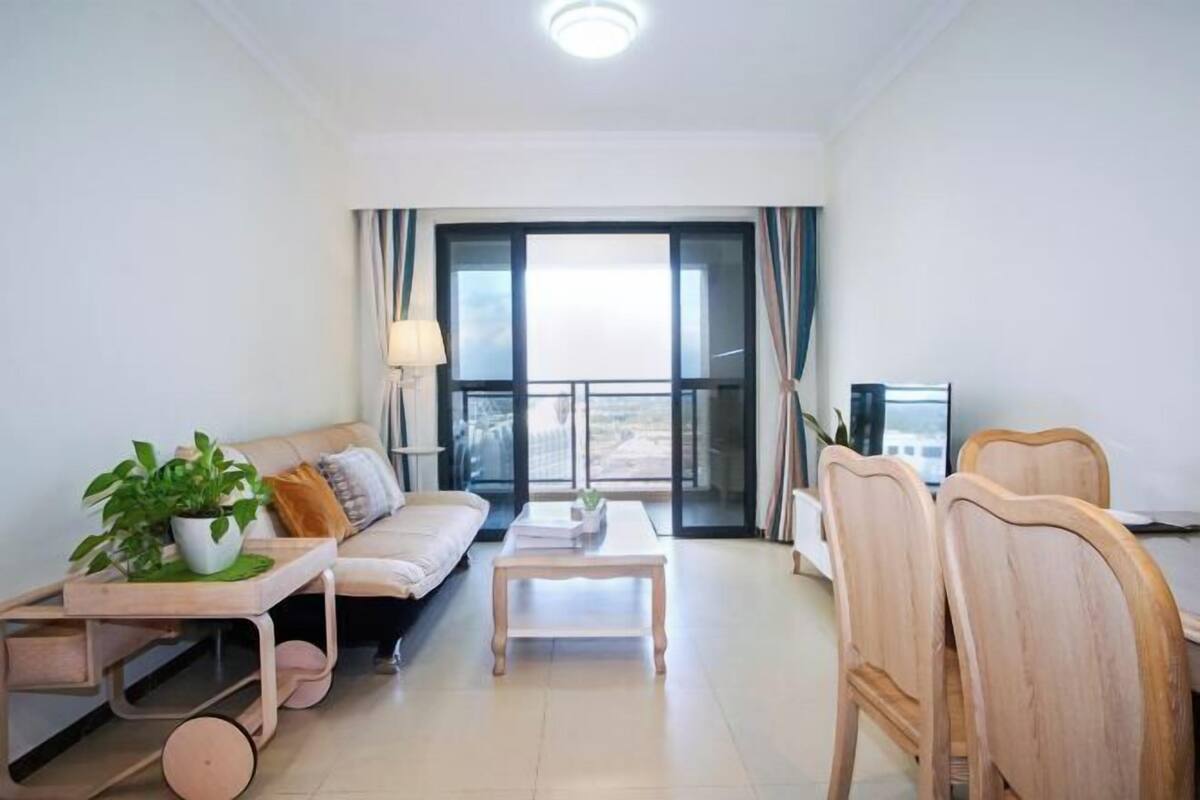 A modern living room with a sofa, coffee table, and chairs, a balcony with curtains, and a potted plant.