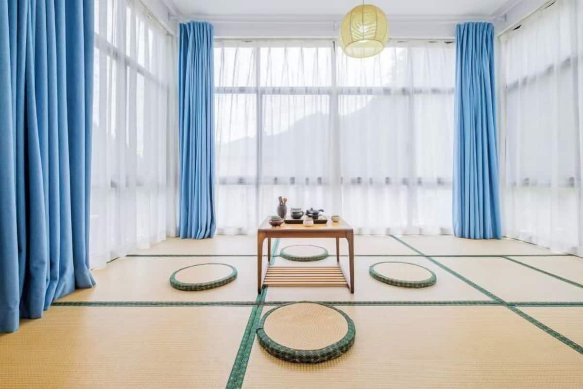 A tatami mat room with a table and tea set, blue curtains, and a hanging light fixture.