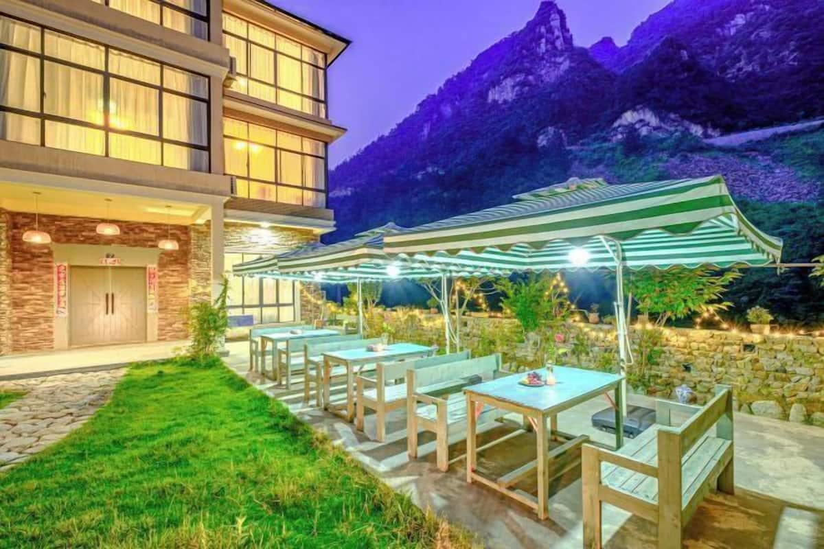 A hotel with outdoor seating, stone walls, and a mountainous backdrop.